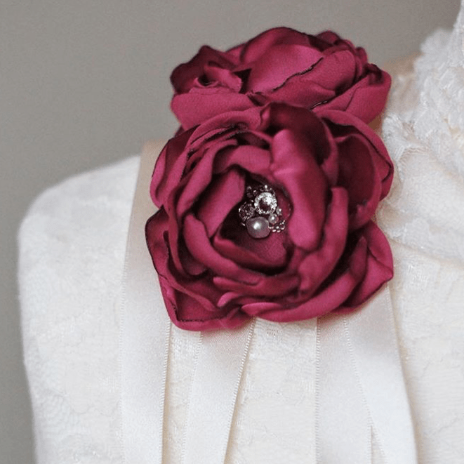 A handmade dark pink fabric flower corsage, resting on a lace-covered mannequin